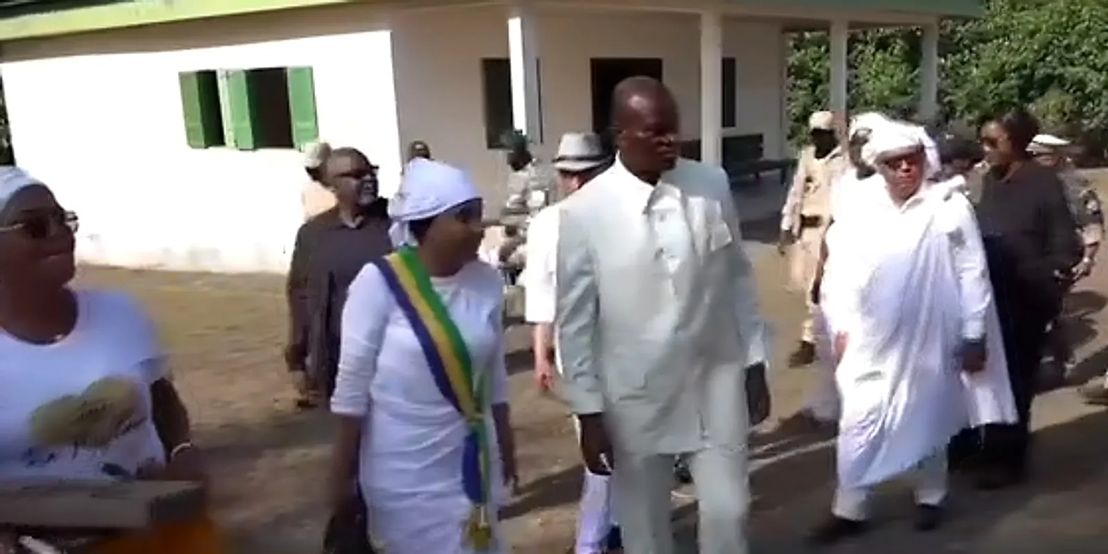Arrival at the King Denis museum: a man in a white suit, an official wearing the sash in the colours of Gabon, women in white and a military escort in front of the building