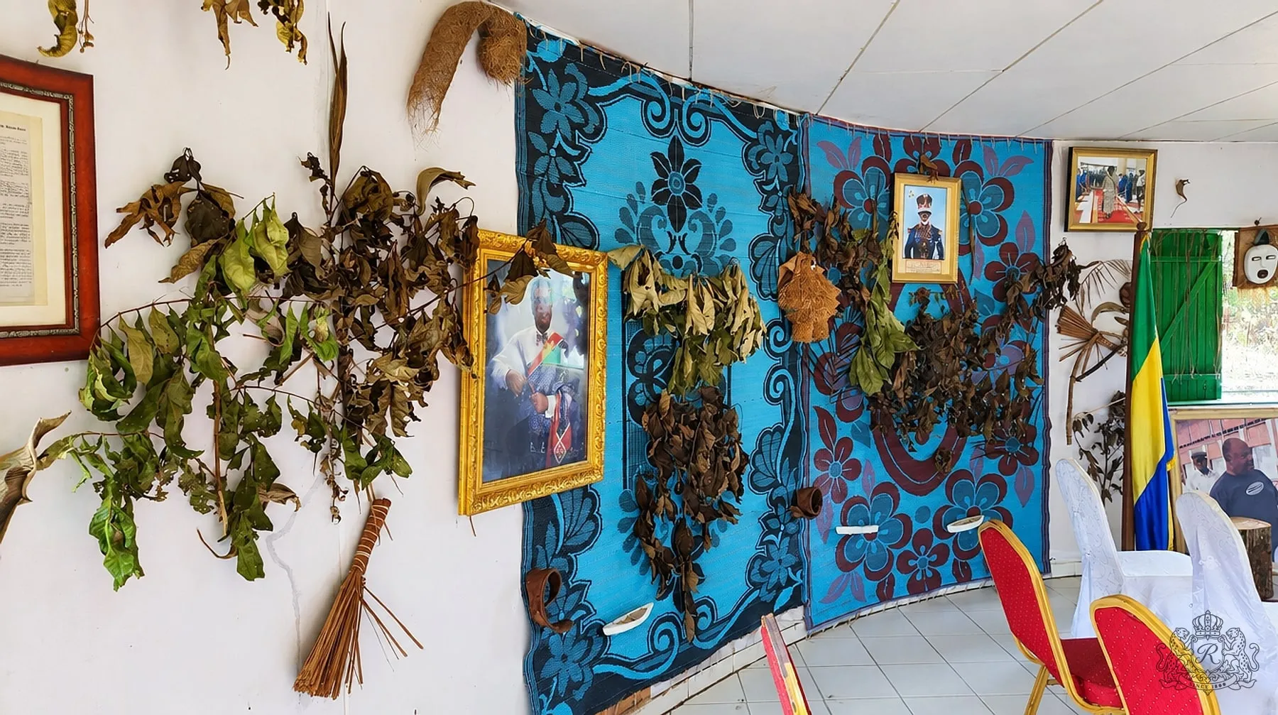 Mur courbe du musée tendu de grandes nattes bleues et bordeaux, portraits encadrés, feuilles rituelles séchées, drapeau gabonais