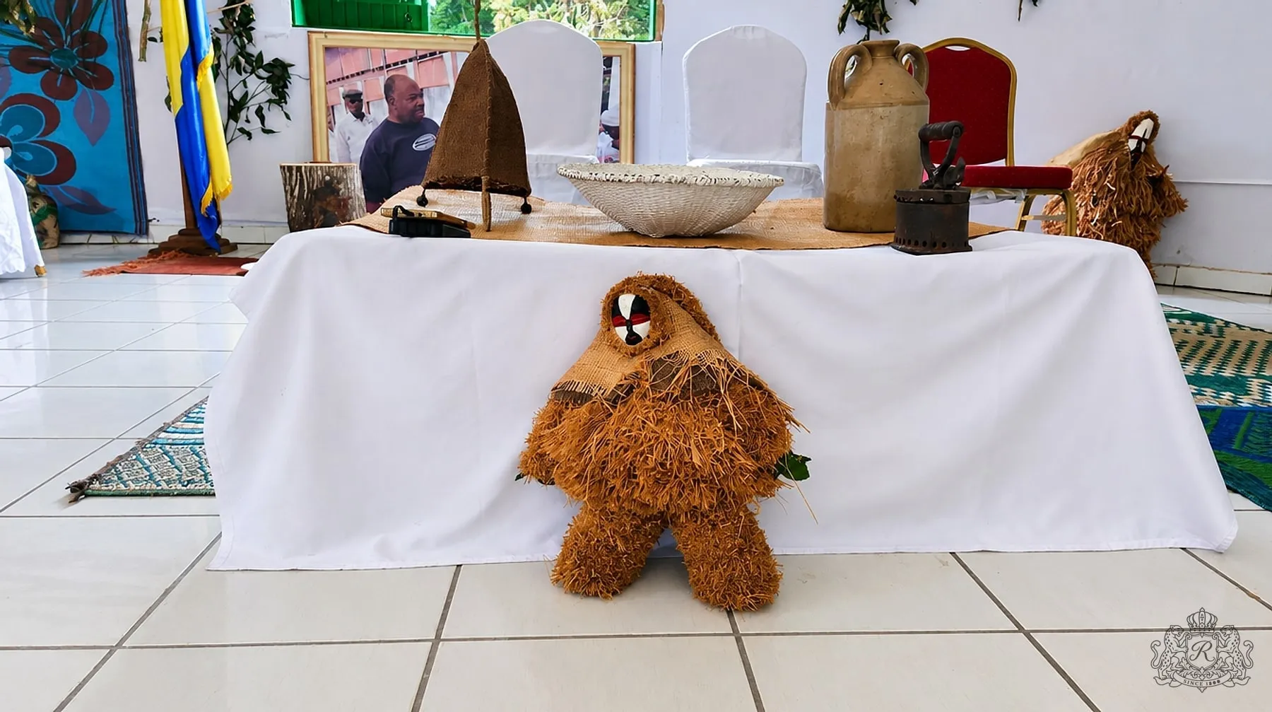 Table des objets anciens gardée par une figure de raphia au masque peint